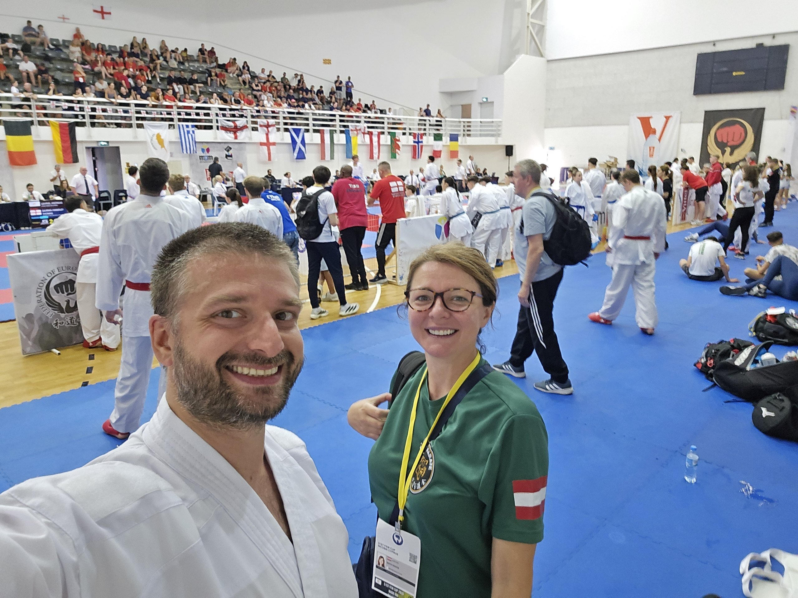 Edvin Kuric im Karategi und Betreuerin Edita Rados in der Halle, im Hintergrund die Flaggen der teilnehmenden Nationen